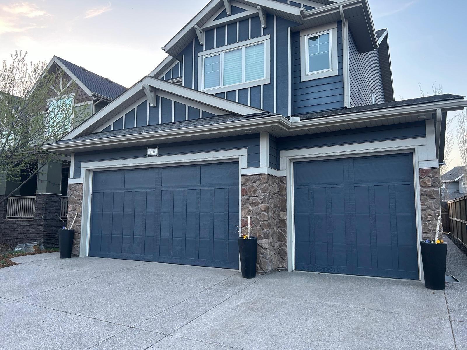 Two-storey home with navy blue siding, white trim and repainted double garage doors