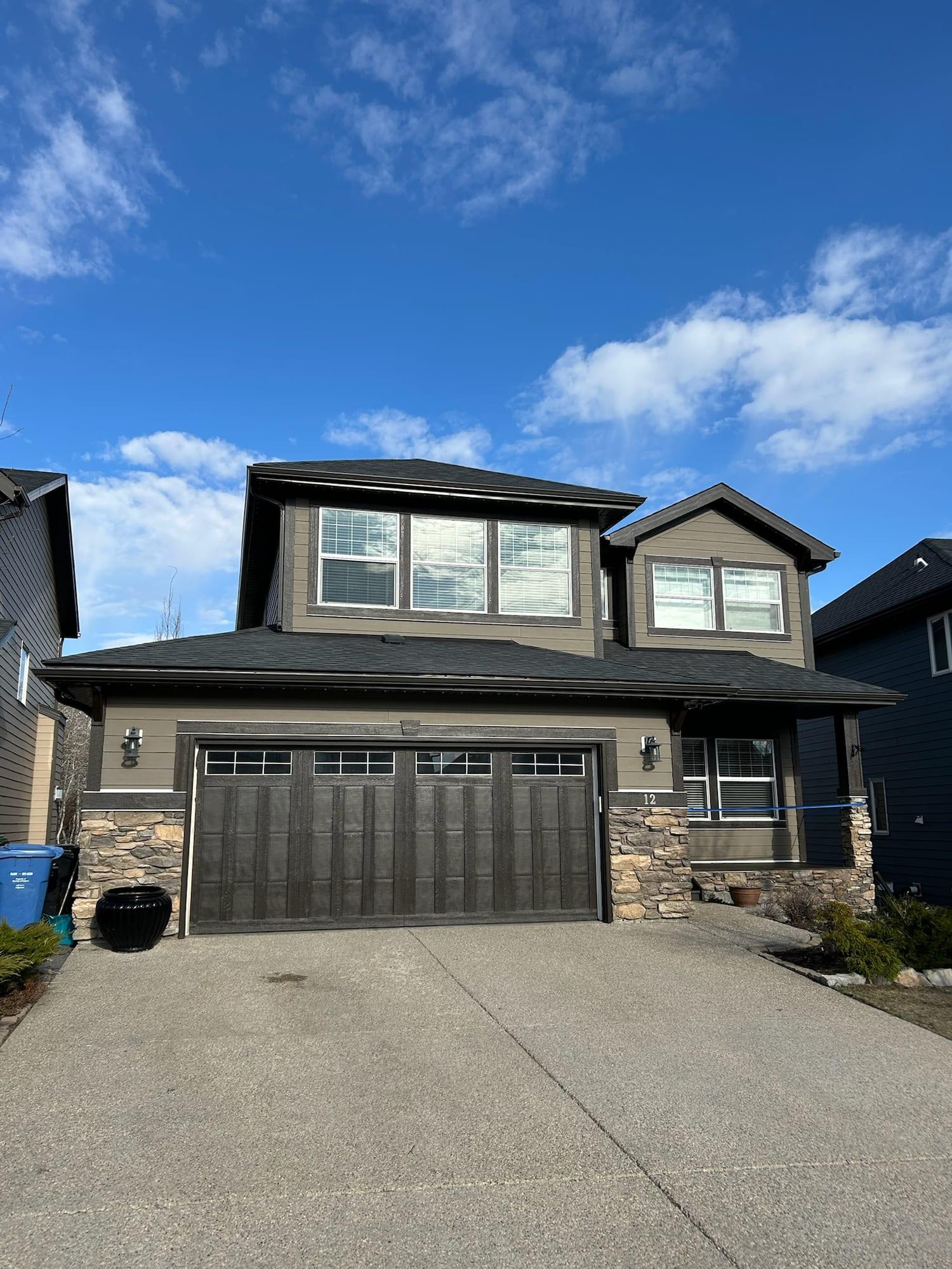 Two-storey home with taupe siding and a dark painted garage door