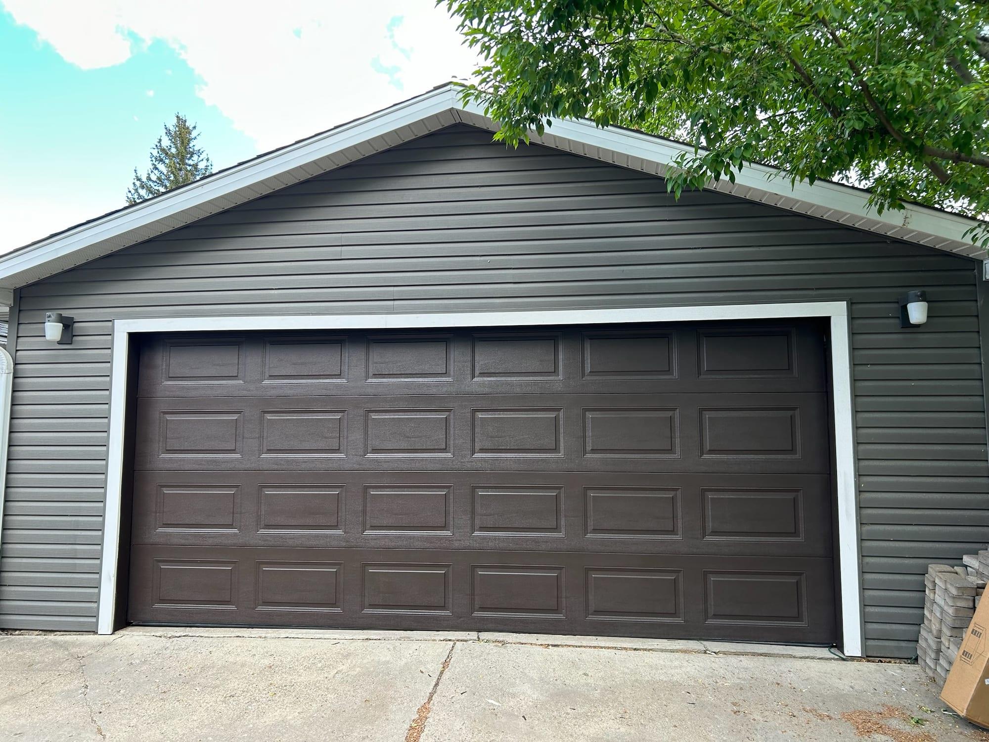 Detached garage with dark brown siding and a matching painted garage door