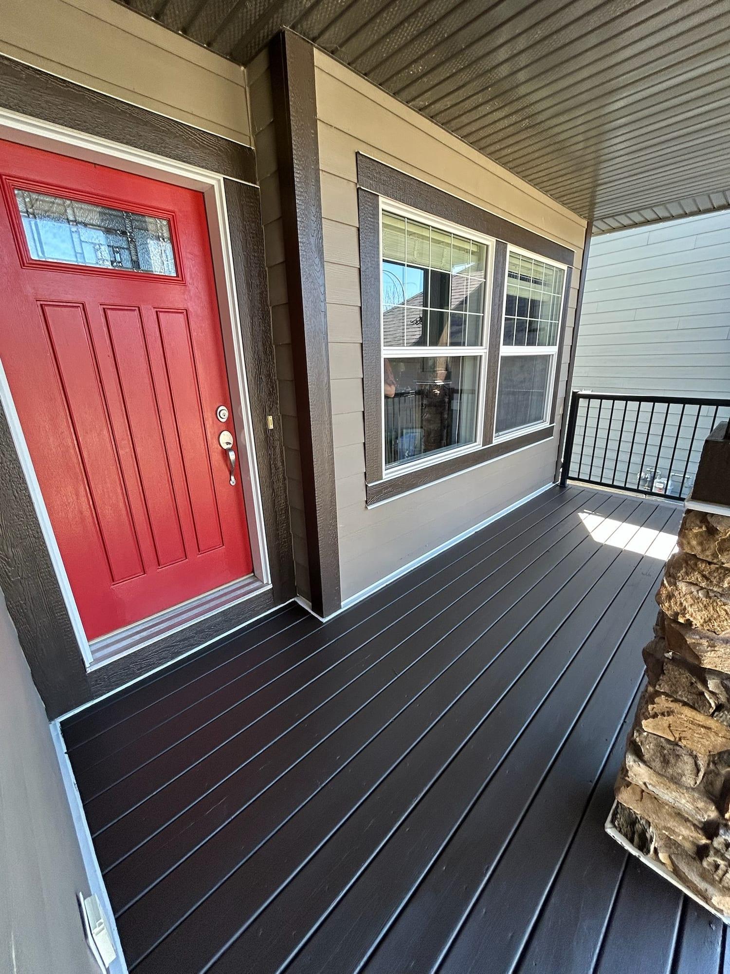 Covered front porch with a red painted door and dark stained decking