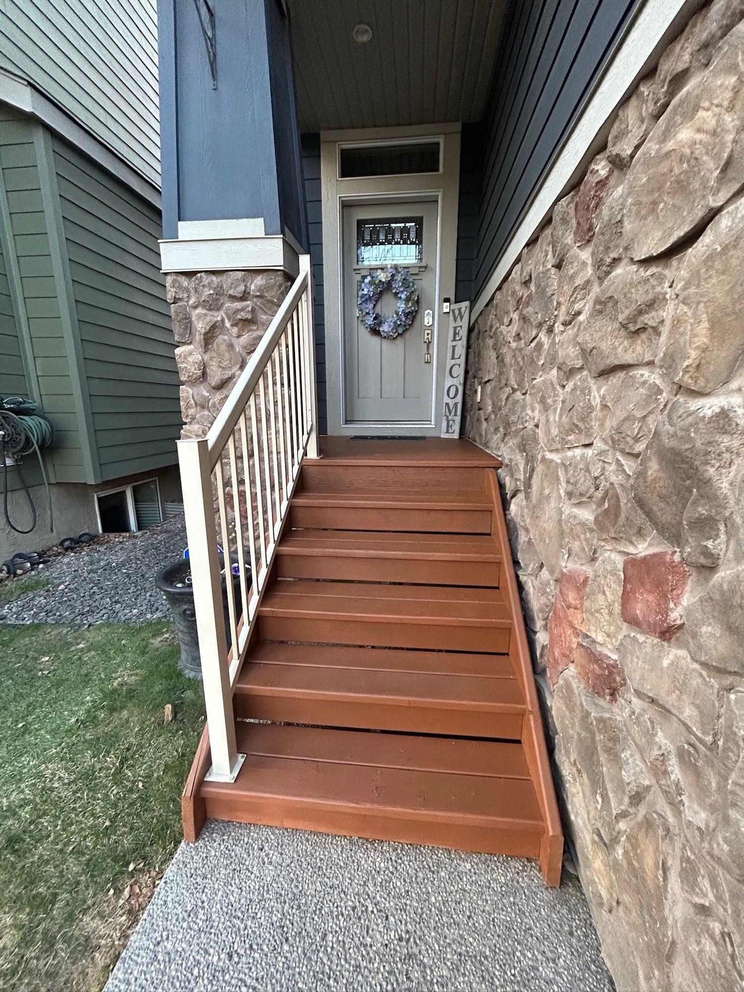 Front steps and landing finished in a warm wood stain, beside white painted railings