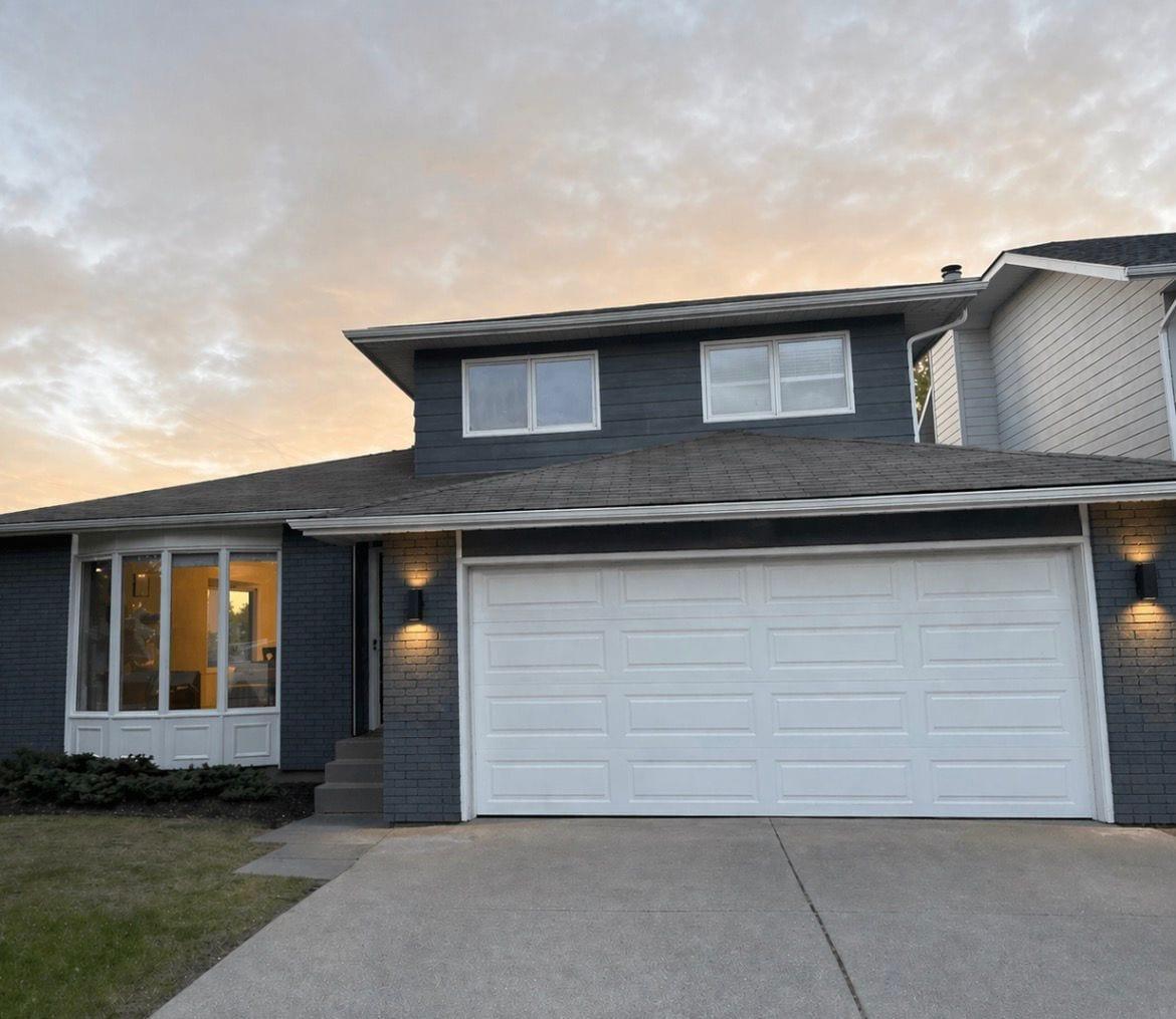 Home exterior painted charcoal with white garage door and window trim, photographed at dusk