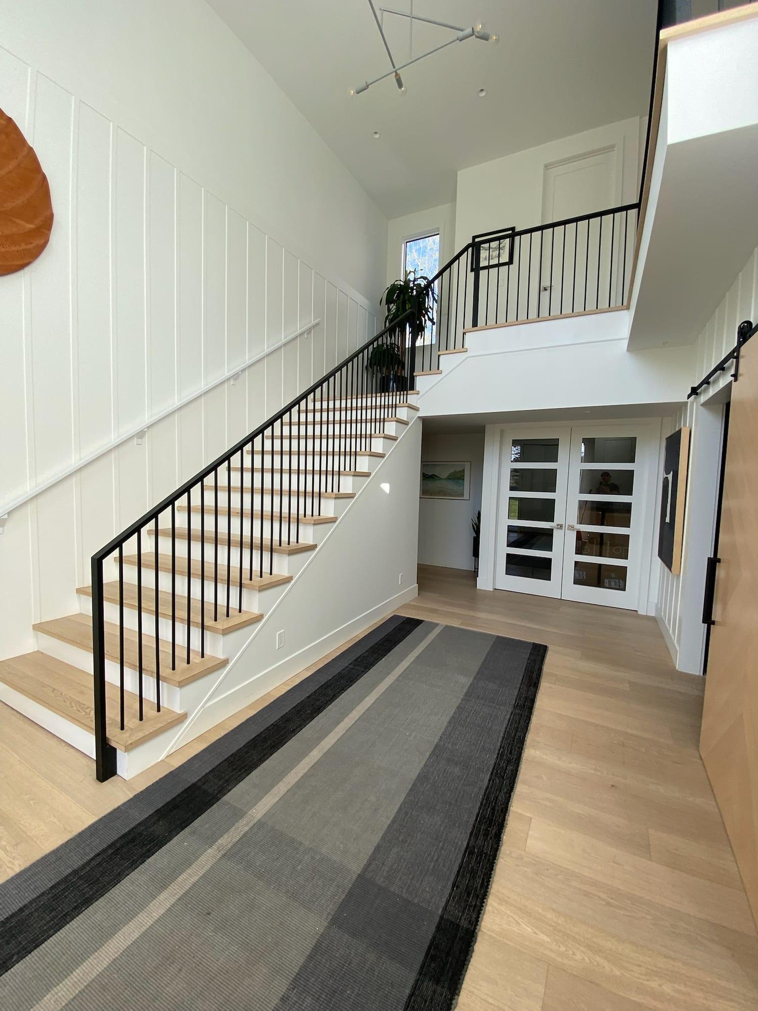 Entryway and stairwell with white walls, a panelled feature wall and black railings